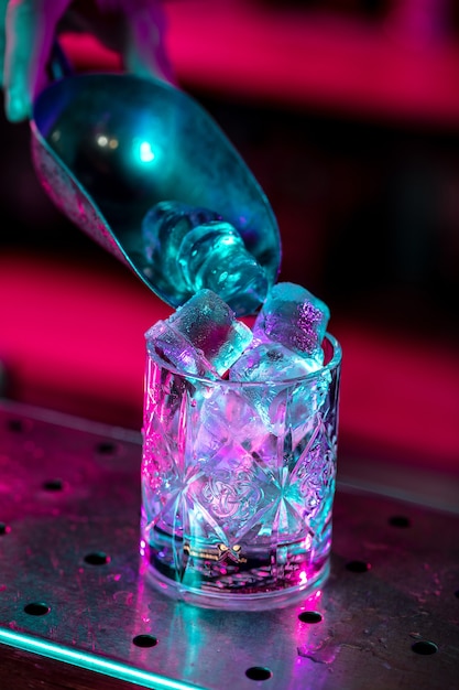 Cerca de cóctel alcohólico, bebida, bebida, vaso lleno de hielo en luz de neón multicolor