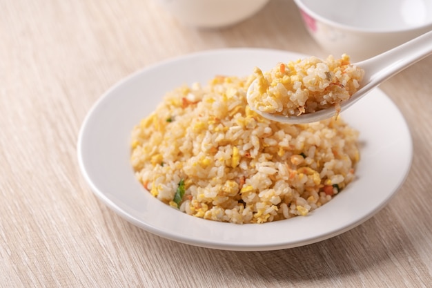 Cerca de comer arroz frito chino con camarones Sakura sergestid en plato blanco sobre la superficie de la mesa de madera brillante.