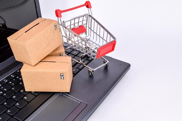 Cerca de la computadora portátil con carrito de compras y cajas de cartón sobre fondo blanco