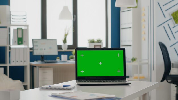 Cerca de la computadora portátil con pantalla verde en la oficina vacía. Nadie en el escritorio con un fondo aislado y una maqueta de la plantilla en la pantalla de croma key. Dispositivo con pantalla de espacio de copia de maqueta en blanco.