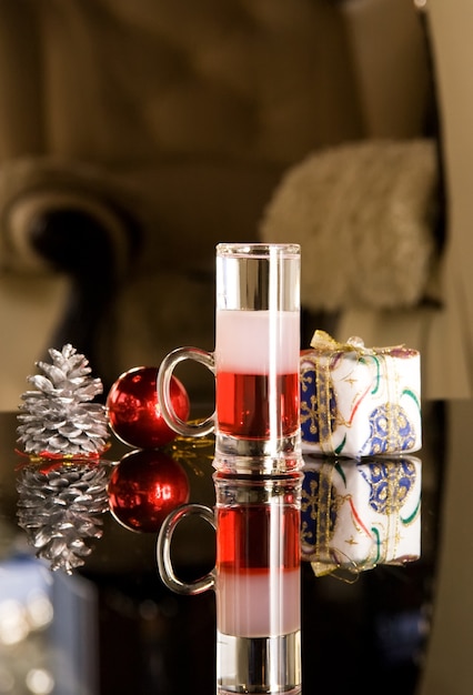Cerca de la copa de cóctel con vodka en la mesa con presente y cono de pino, escena festiva.