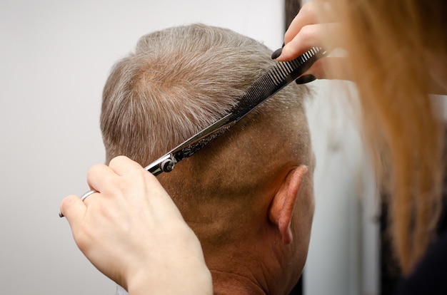 Cerca del corto corte de pelo masculino proceso foran anciano en una barbería.