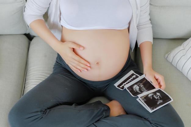 Cerca de la cosecha mujer embarazada asiática es y sosteniendo ultrasonido imagen de escaneo 4D tocando su vientre plan de familia embarazo maternidad personas y expectativa niño y maternidad concepto de atención prenatal