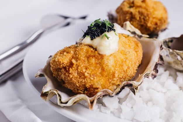 Cerca de la cubierta de ostras fritas con mayonesa y caviar servido en plato blanco