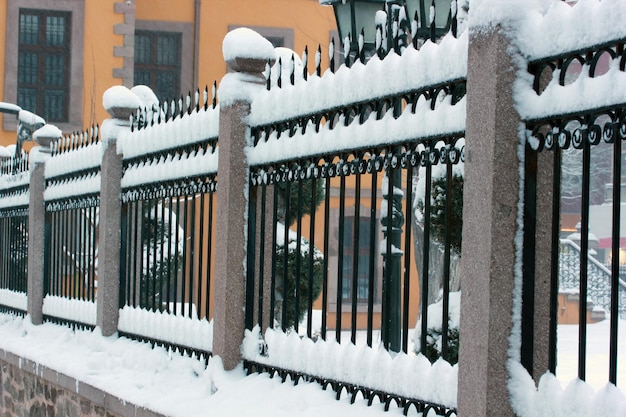 Cerca de ferro coberto de neve do edifício de pedra