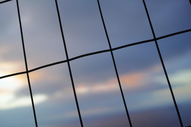 Foto cerca de ferro em linhas horizontais verticais contra um fundo desfocado do céu malha de arame em formas de retângulo para segurança ou conceito de segurança a textura dos padrões de janela ou silhuetas escuras de um portão