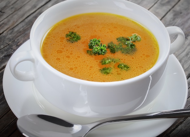 Cerca de delicioso caldo de pollo en una taza de sopa blanca con cuchara