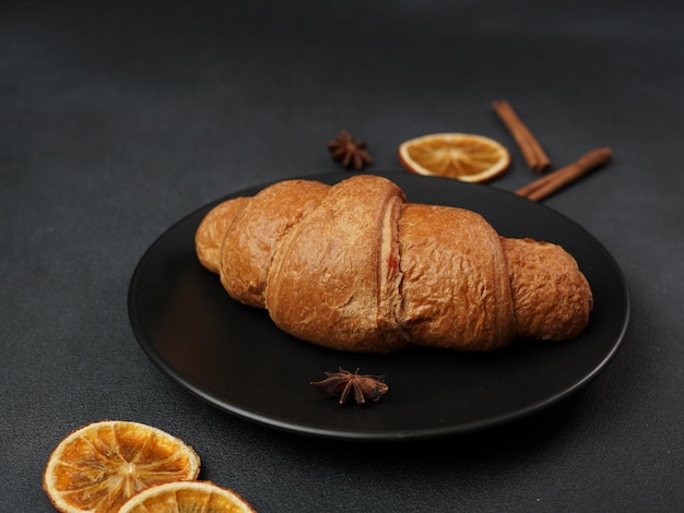 Cerca de un delicioso croissant recién horneado sobre un plato negro sobre un fondo negro