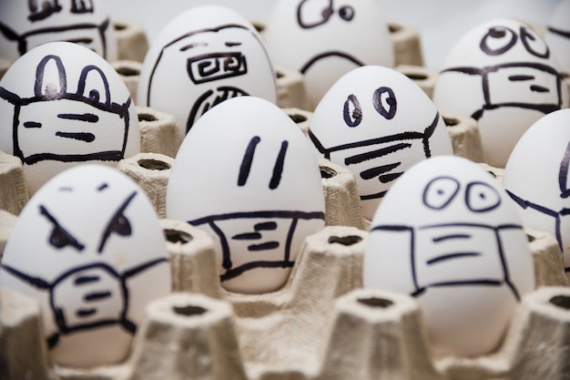 Cerca de diversos huevos de pascua de pollo con caras emocionales de doodle con máscaras médicas con blanco