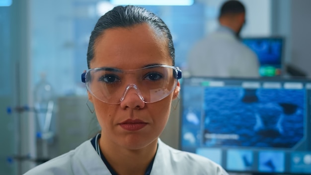 Cerca del doctor científico cansado mirando a la cámara sonriendo trabajando en laboratorio equipado. Químico que examina la evolución del virus utilizando herramientas de alta tecnología y química para la investigación científica, el desarrollo de vacunas