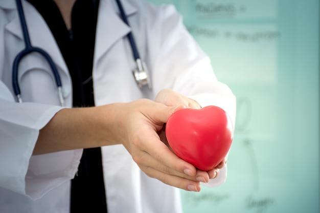 Cerca del doctor de la mujer joven que sostiene un corazón rojo