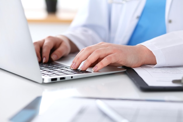 Cerca de una doctora desconocida escribiendo en una computadora portátil mientras está sentada en la mesa. Personal médico, concepto de trabajo obligatorio.