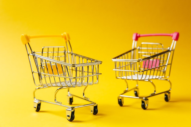 Cerca de dos carros de empuje de supermercado para compras con ruedas y elementos de plástico amarillo y rosa en el mango aislado sobre fondo amarillo. Concepto de compras. Copie el espacio para publicidad.