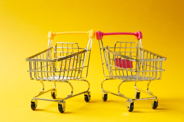 Cerca de dos carros de empuje de supermercado para compras con ruedas y elementos de plástico amarillo y rosa en el mango aislado sobre fondo amarillo. Concepto de compras. Copie el espacio para publicidad.