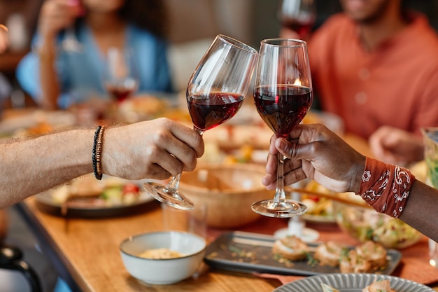 Cerca de dos personas tintineando copas de vino durante la cena en un acogedor espacio para copiar