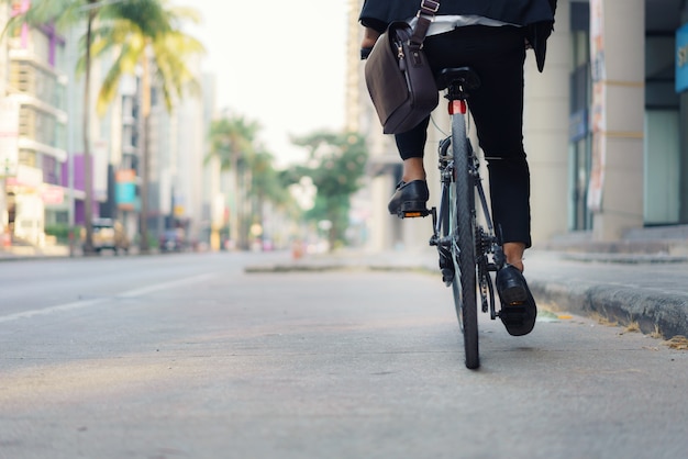 Cerca del empresario de pie está montando una bicicleta en las calles de la ciudad para su viaje matutino al trabajo. Concepto de transporte ecológico.