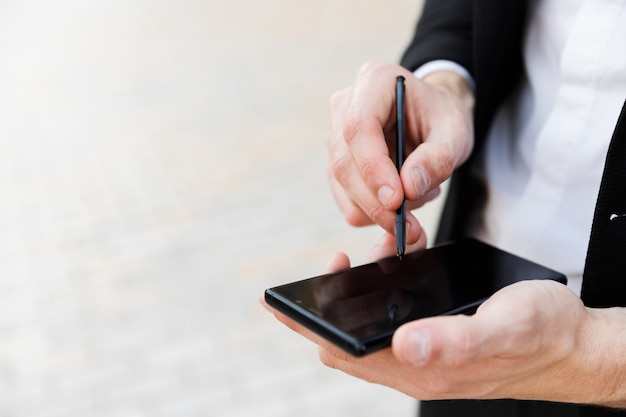 Cerca de un empresario mediante teléfono móvil y lápiz óptico al aire libre