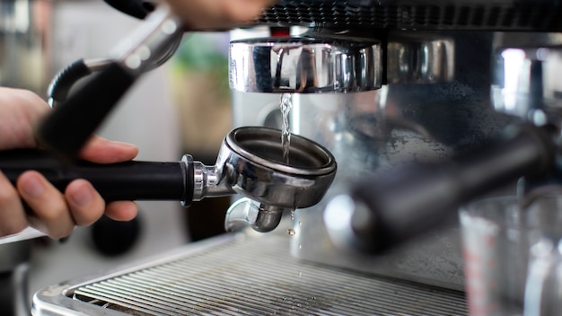 Cerca de enjuague con agua tibia en el vertido de la máquina de café. Un hombre barista preparándose para presionar café molido para preparar espresso o americano en una cafetería.