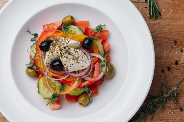 Cerca de ensalada griega con verduras frescas, queso feta y aceitunas en un plato vegetariano saludable