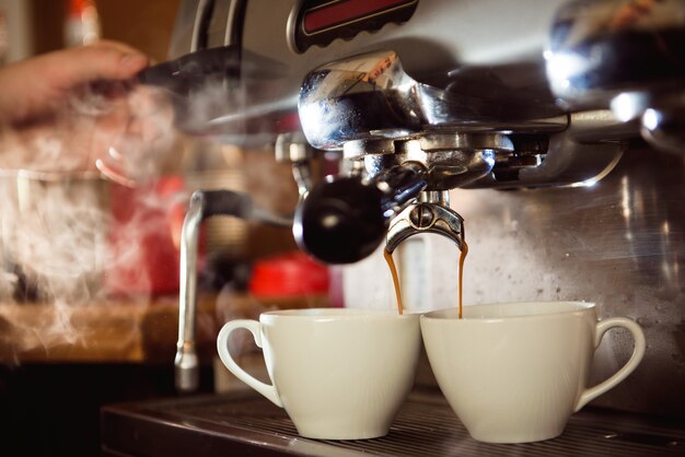 Cerca de espresso de la máquina de café en dos tazas blancas. Elaboración de capuchino profesional.