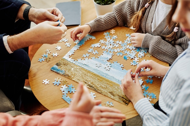 Cerca de una familia irreconocible jugando al juego de rompecabezas juntos en casa