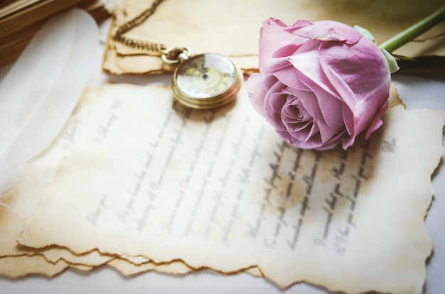 Foto cerca de flor color de rosa con reloj de bolsillo antiguo y cartas de amor con tono vintage