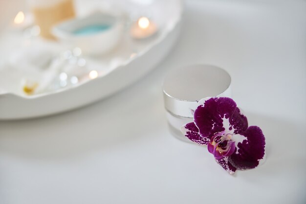 Cerca de la floración de la orquídea violeta y una pequeña vela perfumada en el cuadro blanco