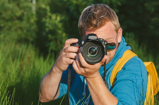 Foto de cerca, el fotógrafo sostiene una cámara de video y fotografía profesional en sus manos. en el contexto de la hermosa naturaleza verde.