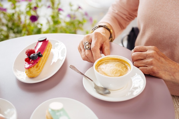 Cerca de la frágil taza de porcelana llena de café y canutillos colocando sobre la mesa