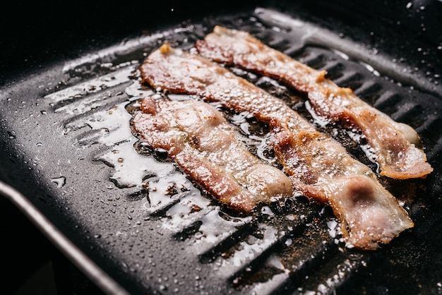 Cerca de freír tiras de tocino chisporroteando en una sartén con aceite de tocino engrasado caliente