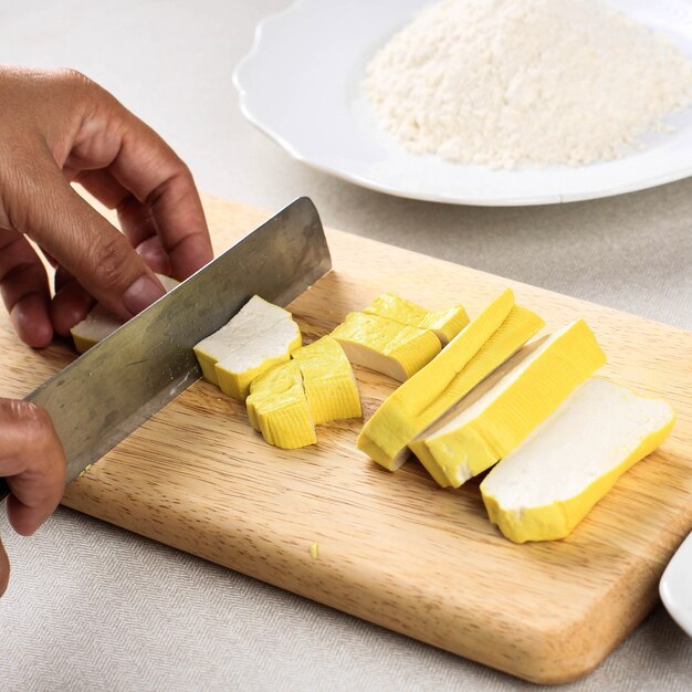 Cerca de frijol crudo tofu amarillo Bandung cortando en cubo con un cuchillo sobre una tabla de madera