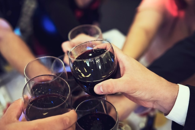 Cerca de gente tintineo de vasos encima de la mesa del restaurante. Brindis en una velada de banquete. Celebración con bebidas en una cena. Hombres y mujeres festejan un evento. Un brindis.