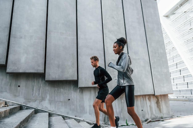 Cerca de la gran pared, el hombre europeo y la mujer afroamericana con ropa deportiva hacen ejercicio juntos