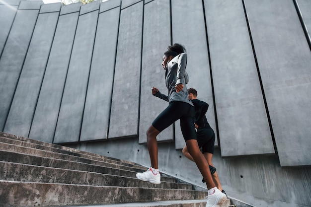 Foto cerca de la gran pared, el hombre europeo y la mujer afroamericana con ropa deportiva hacen ejercicio juntos