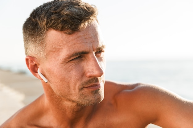 Cerca de guapo deportista sin camisa con auriculares