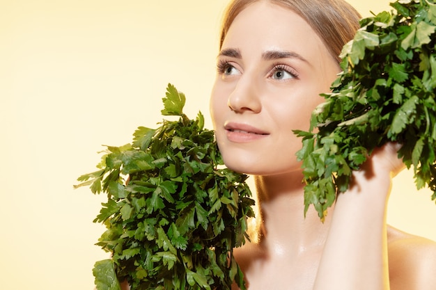 Cerca de la hermosa joven con hojas verdes sobre fondo blanco.