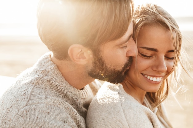 Cerca de una hermosa joven pareja sonriente abrazando mientras está de pie en la playa