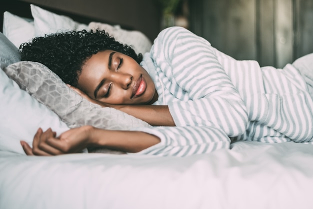 Cerca de una hermosa mujer negra con cabello rizado durmiendo en la cama con los ojos cerrados