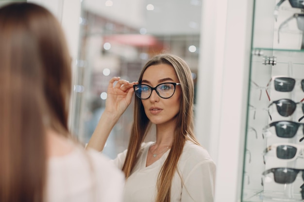 Cerca de hermosa mujer sonriente joven sonriendo recogiendo y eligiendo anteojos en la esquina del óptico en el centro comercial feliz hermosa mujer comprando anteojos en el optometrista