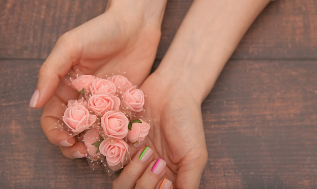 De cerca. Hermosas manos femeninas con manicura moderna y flores rosadas.