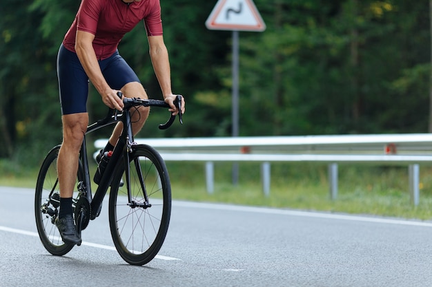 Cerca del hombre activo en ropa deportiva y zapatillas de ciclismo en carretera pavimentada. Centrarse en piernas musculosas y fuertes