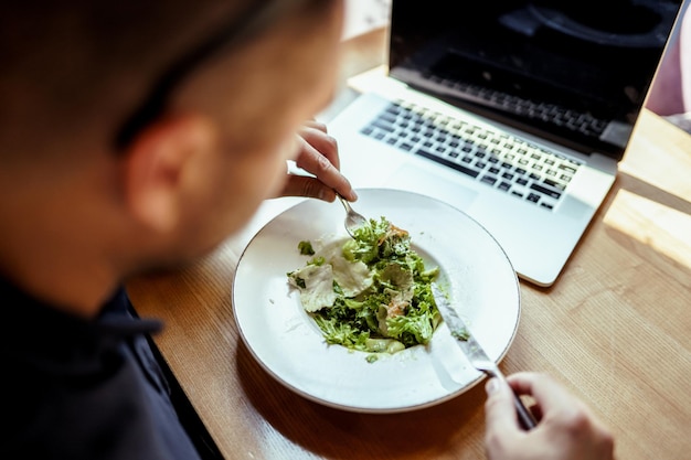 Cerca del hombre almorzando en un restaurante en frente de la computadora portátil