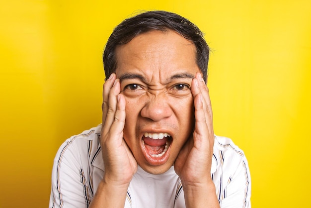 Cerca del hombre asiático enojado gritando aislado sobre fondo amarillo