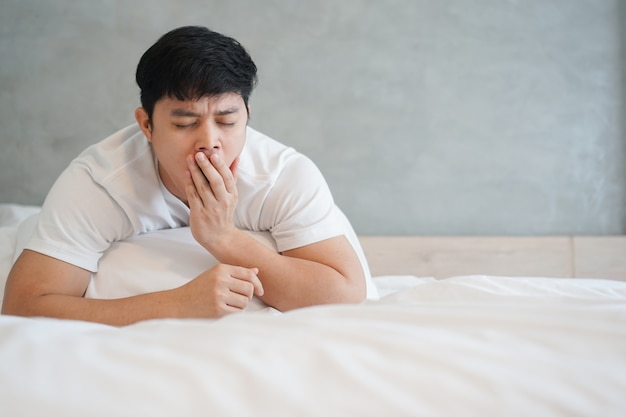 de cerca hombre asiático soñoliento y bostezando en el dormitorio en día de vacaciones