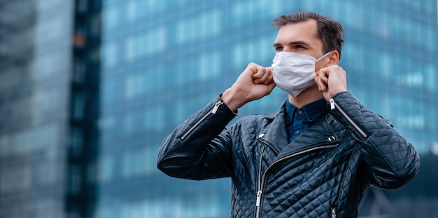 De cerca. hombre atractivo poniéndose una máscara protectora en una calle de la ciudad. concepto de protección de la salud