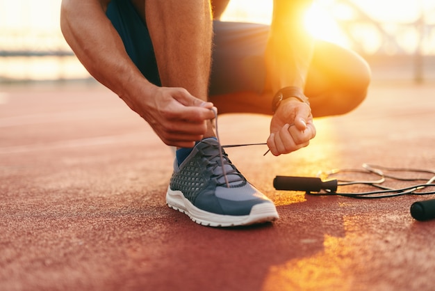 Cerca del hombre deportivo atar cordones de los zapatos mientras arrodillado en un tribunal en la mañana