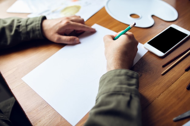 Cerca del hombre dibujando con pinturas y lápices en casa. Ambiente confortable. Educación a distancia, ocupación creativa, arteterapia. Digitalización, utilizando diferentes dispositivos, gadgets. Copyspace.