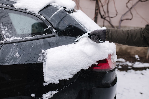 Cerca del hombre está limpiando la ventana nevada de un coche con un raspador de nieve. Concéntrese en el raspador. Frío