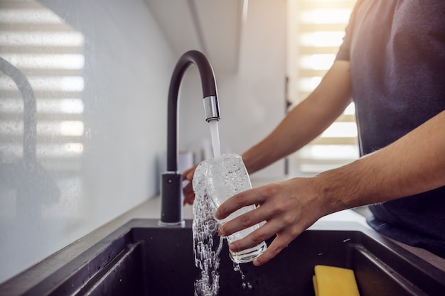 Cerca del hombre llenando el vaso con agua fresca del grifo.