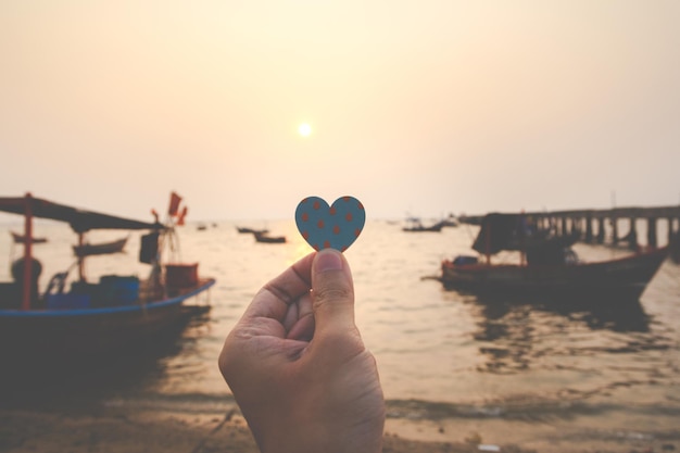 Cerca del hombre de la mano que sostiene un corazón de papel con el fondo del mar por la noche. concepto de amor, feliz san valentín.